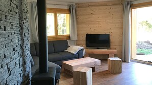 A modern living room with a stone wall, a sofa, a TV, and a wooden coffee table. - Chalet Le Lynx (Ferdrupt)