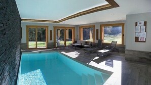 A modern indoor swimming pool with clear glass walls, a stone wall, and a view of the outdoors. - Chalet Le Lynx (Ferdrupt)