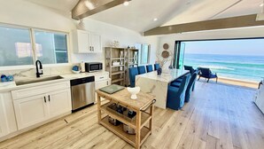 Una cocina moderna con piso de madera, un comedor con sillas azules y vista al océano.