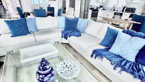 Un salón moderno con una mesa de centro de vidrio, sofás blancos y cojines azules.
