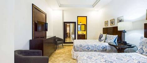 A hotel room with two beds, a desk, a chair, a ceiling fan, and a TV.