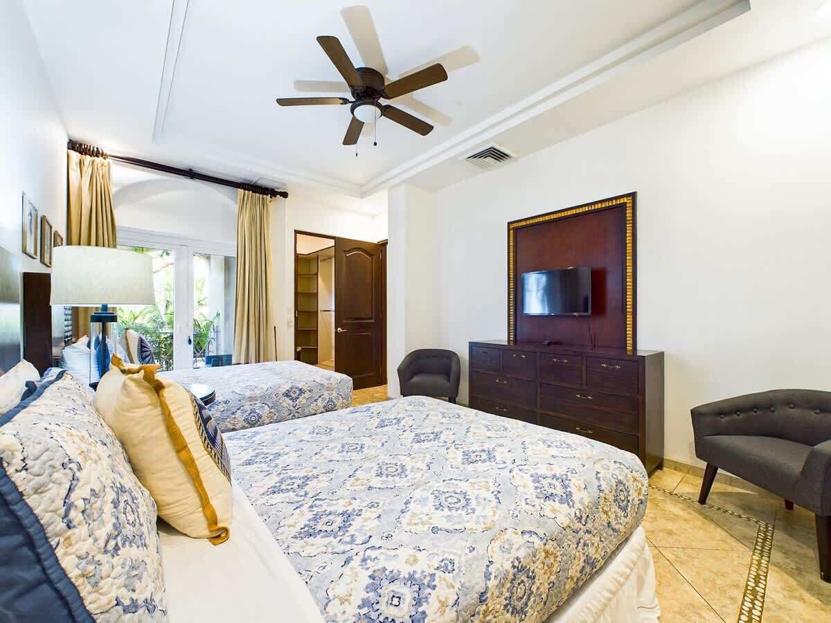 Een hotelkamer met twee bedden, een plafondventilator, een televisie, een dressoir en een stoel.