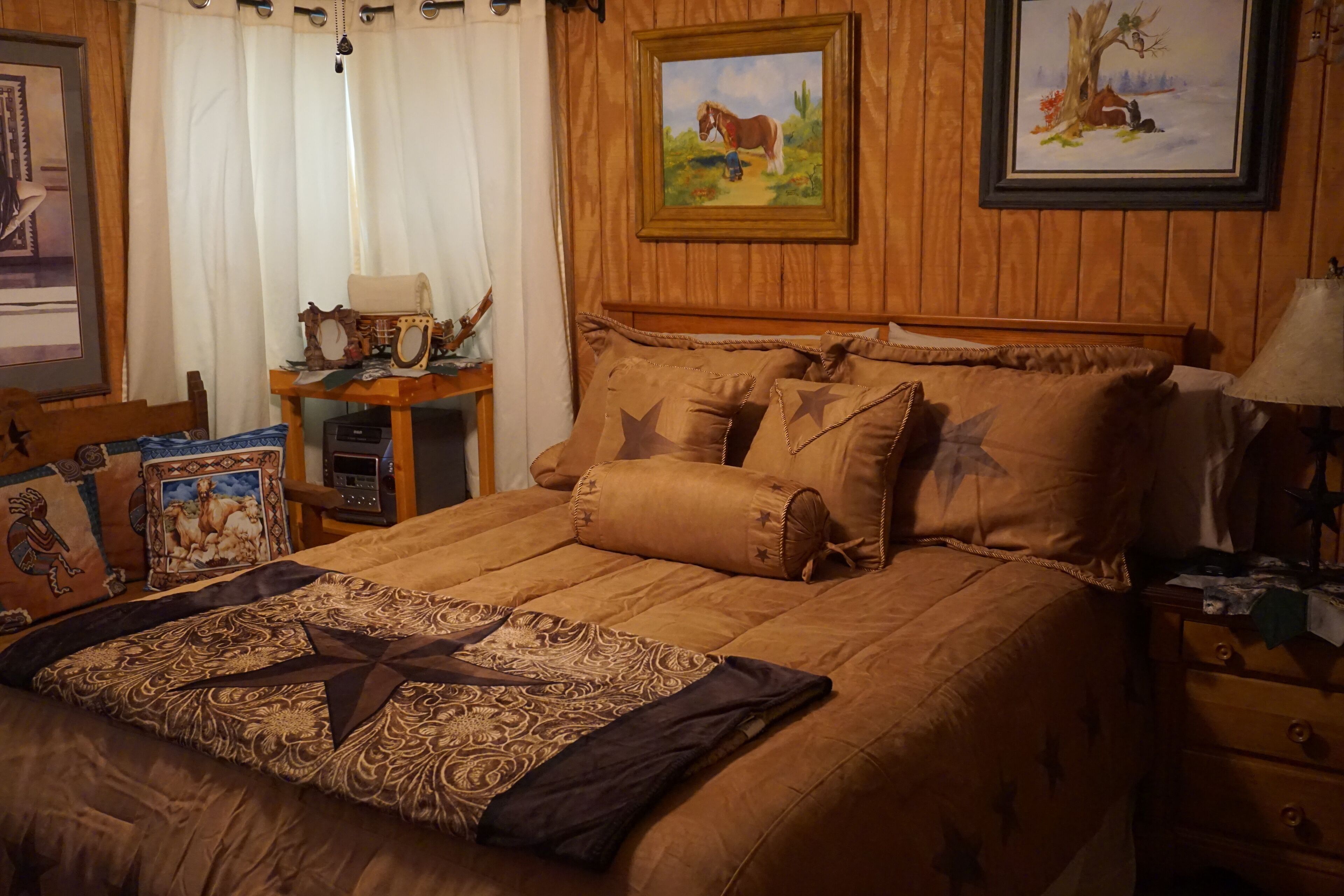 Un dormitorio acogedor con cabecera de madera, cama con ropa de cama marrón, mesita de noche con lámpara y dos cuadros en la pared.