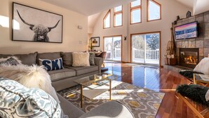 A spacious living room with a large window, a fireplace, and a mounted TV. - Quiet Vermont Winter Getaway (Bridgewater)