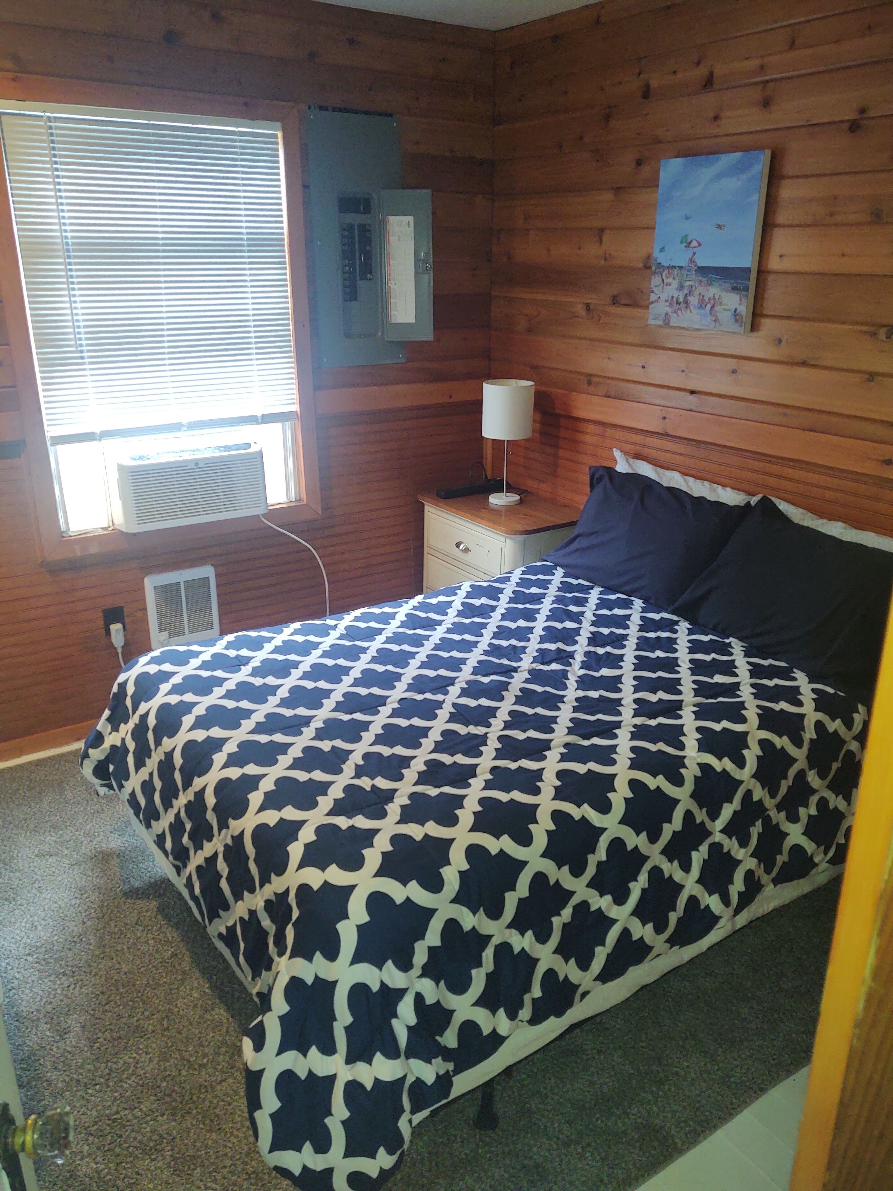 Une chambre à coucher comprenant un lit, une table de chevet, une lampe, une fenêtre avec des stores et un radiateur fixé au mur.