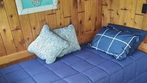 Una habitación con pared de madera, una cama con ropa de cama azul, almohadas estampadas y un cuadro enmarcado en la pared.