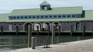 Un edificio frente al agua con techo verde, múltiples ventanales y un muelle que se extiende sobre el agua.