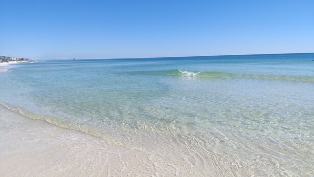 Een strand met helder ondiep water en een pier in de verte.