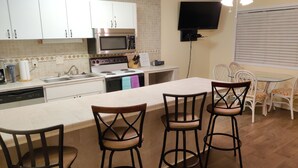 Een keuken met een magnetron, fornuis, spoelbak en een eethoek met stoelen en een tafel.