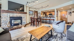 A spacious living room with a stone fireplace, a dining area, and a kitchen with bar stools. - Remodeled unit & mountain view in the ♥ of Central Village, walk to the lifts!  (Frisco)