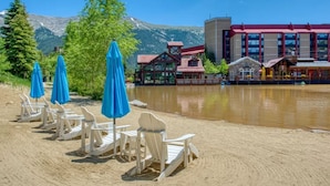 A lakeside resort with wooden chairs and blue umbrellas, a building with a red roof, and mountains in the background. - Remodeled unit & mountain view in the ♥ of Central Village, walk to the lifts!  (Frisco)