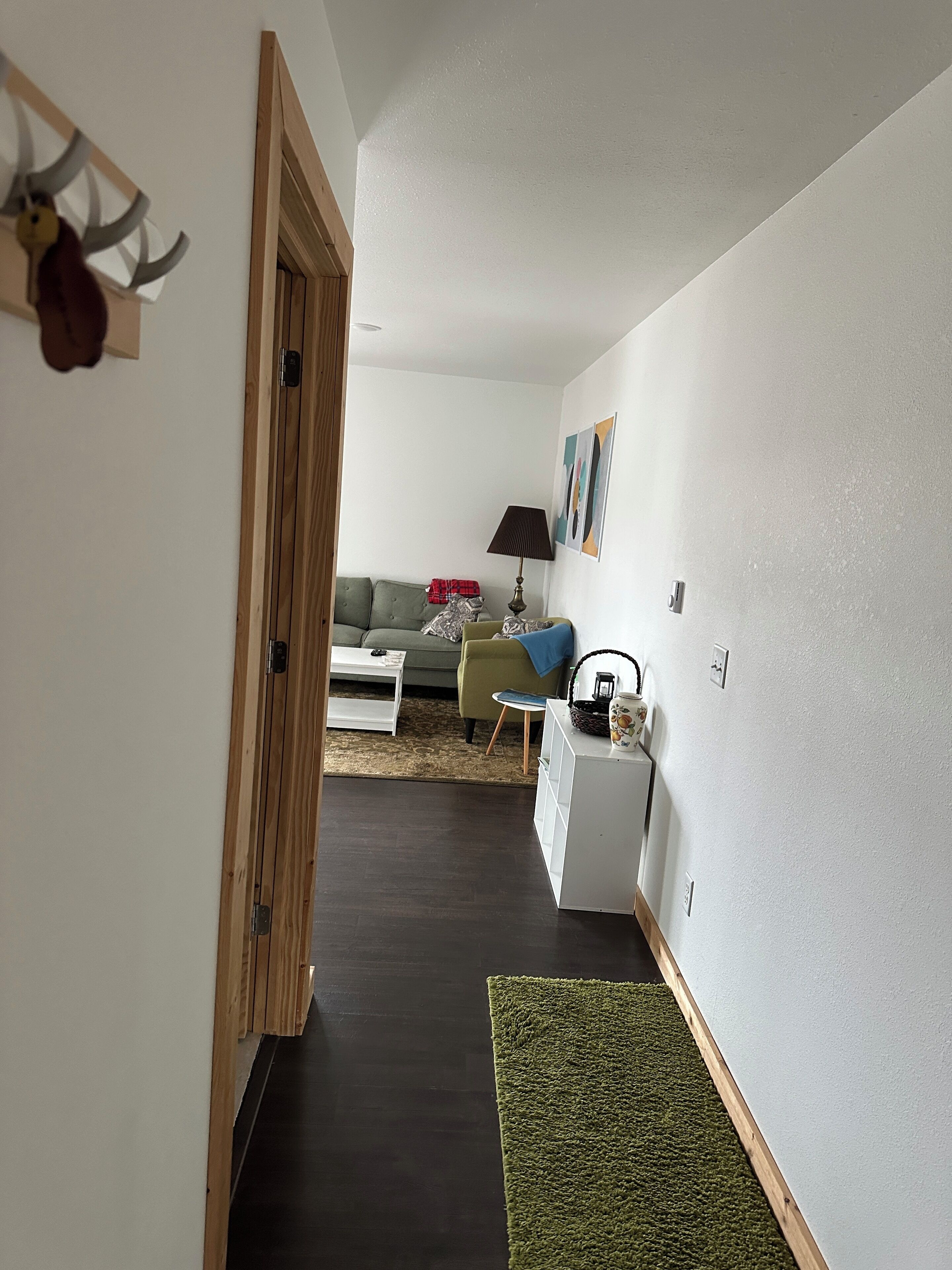 Un pasillo que conduce a una sala de estar con un sofá verde, una mesita auxiliar blanca y una lámpara.