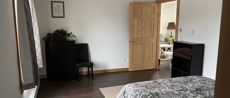 A bedroom with a bed, a desk, a chair, a wardrobe, and a door leading to another room.