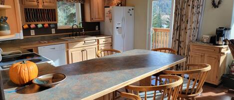 A kitchen with wooden cabinets, a central island with bar stools, a refrigerator, and a window with curtains.