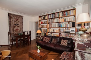A living room with a leather sofa, a wooden coffee table, a bookshelf, and a dining area with a table and chairs. - Charming Maître Albert 2BR/2BA near Seine, St. Germain and Notre-Dame (Paris)