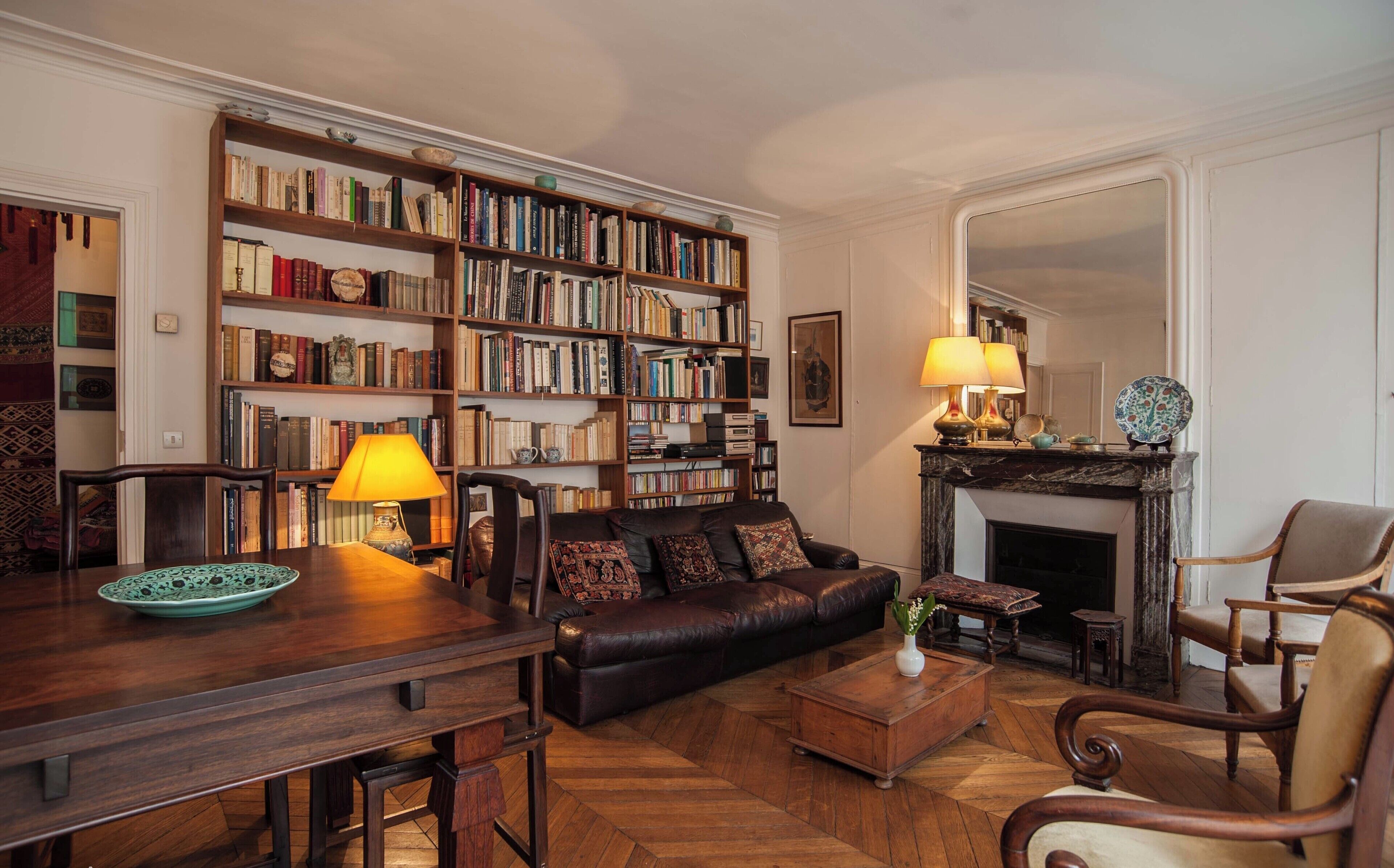 Una sala de estar acogedora con un sofá de cuero, una mesa de centro de madera y una chimenea. Una amplia estantería llena de libros recubre la pared.