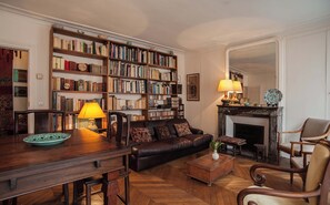 A cozy living room with a leather sofa, a wooden coffee table, and a fireplace. A large bookshelf filled with books lines the wall. - Charming Maître Albert 2BR/2BA near Seine, St. Germain and Notre-Dame (Paris)