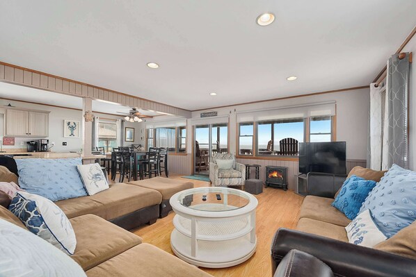 A spacious living area with a sofa set, a round coffee table, and a fireplace. - OBX Life I. Wake to Ocean front Sunrises, Walk to the Pier, Private Pool (Nags Head)