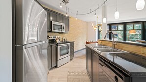A modern kitchen with stainless steel appliances, a large island, and a view of the outdoors through the windows. - Ski-In/Ski-Out Corner Unit 2BR/2BA Mountain Views & In-Unit Laundry (Salt Lake City)