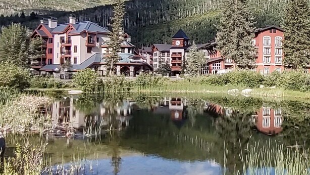 A lakeside hotel with multiple buildings, including a clock tower, surrounded by forested hills. - Ski-In/Ski-Out Corner Unit 2BR/2BA Mountain Views & In-Unit Laundry (Salt Lake City)