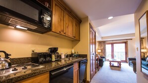 A kitchen with granite countertops, wooden cabinets, a stove, a dishwasher, and a microwave. There is a dining area with a table and chairs, and a balcony with a view. - Modern Studio Condo | Fireplace and Balcony (Crested Butte)