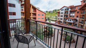 A balcony with a view of multi-story buildings, outdoor seating, and a wooden railing. - Modern Studio Condo | Fireplace and Balcony (Crested Butte)