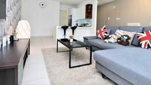 A modern living room with a grey sofa, a black coffee table, and a kitchen in the background. - Executive 3 BR Condo, Cyberjaya (Cyberjaya)