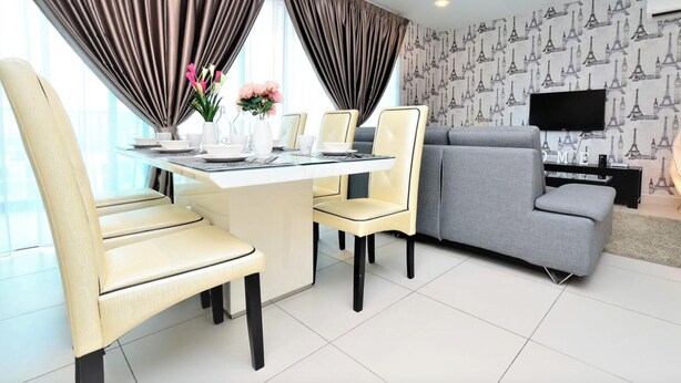 A modern living room with a grey sofa, a dining table with chairs, and a TV on a stand. - Executive 3 BR Condo, Cyberjaya (Cyberjaya)