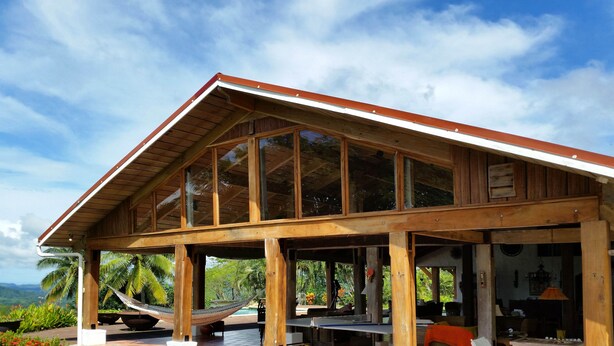 Un bâtiment en bois doté de grandes fenêtres, d’un hamac et d’un espace piscine.