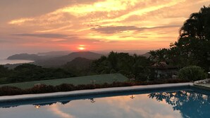 Une piscine avec vue sur le coucher de soleil, entourée de verdure et de collines.