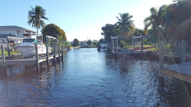 A marina with boats docked, a waterway, and palm trees. - Home Away from Home with Gulf Access and Heated Pool (Cape Coral)