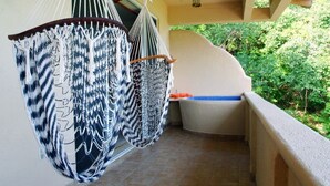 A balcony with two macramé hammocks, a bathtub, and a view of greenery.