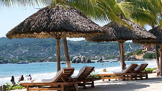 A beach with wooden lounge chairs and thatched umbrellas.