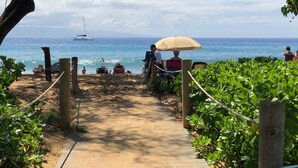 A beach path leading to the sea with people sitting under umbrellas. - Wow!-Best of HK-Inner Courtyard-Ocean Views-Steps to Beach & Pool-100+ Reviews (Lahaina)