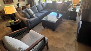 A living room with a sectional sofa, a small table, a coffee table, a floor lamp, and a ceiling fan. - Wow!-Best of HK-Inner Courtyard-Ocean Views-Steps to Beach & Pool-100+ Reviews (Lahaina)