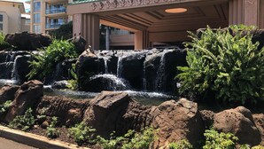 A hotel entrance with a waterfall feature, a stone pathway, and lush greenery. - Wow!-Best of HK-Inner Courtyard-Ocean Views-Steps to Beach & Pool-100+ Reviews (Lahaina)