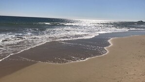 Une plage où les vagues viennent doucement lécher le rivage sous un ciel dégagé.