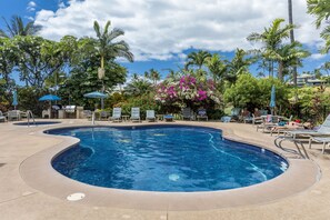 Une piscine entourée de palmiers et de plantes tropicales, avec des chaises longues et des parasols.