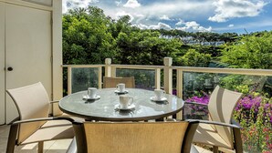 Een ronde tafel met stoelen op een balkon, met uitzicht op een weelderige tuin en een verafgelegen panorama.
