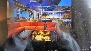 A modern lounge area with a glass-top fire pit, orange seating, and blue umbrellas. - Spring Discounts! Big Yard for Pets! Restaurants!BROADWAY/Downtown 1 ML TOPGOLF! (Nashville)
