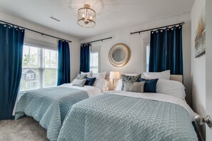 Two queen-sized beds are dressed in light blue quilted bedspreads, complemented by a large round mirror and a contemporary light fixture.