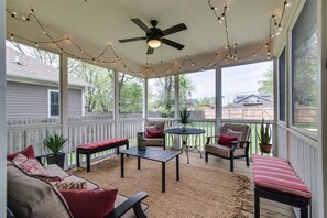 Relax in this serene outdoor space with a ceiling fan, comfortable seating, and lush greenery.