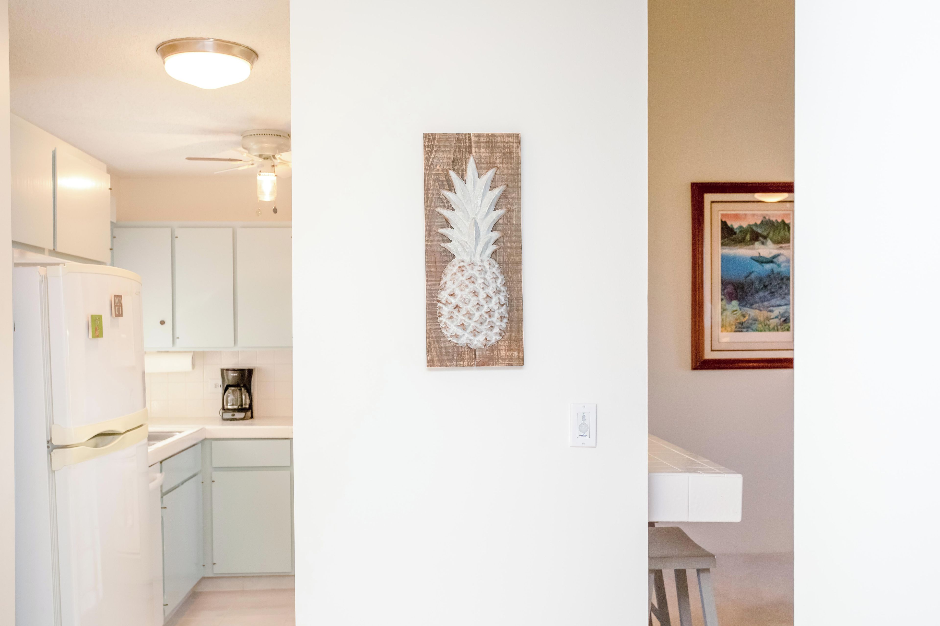 A kitchen with white cabinets, a coffee maker, and a pineapple artwork on the wall.