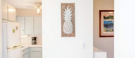 A kitchen with white cabinets, a coffee maker, and a pineapple artwork on the wall.