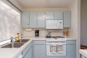A kitchen with light blue cabinets, a white microwave, a stove, and a sink.