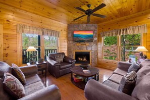 A cozy cabin interior with wooden walls, a stone fireplace, leather sofas, and a ceiling fan. - Gatlinburg, Hot Tub, Huge Arcade, Dual Racing, Theater, Walk-2-Pool, Free Tix (Gatlinburg)