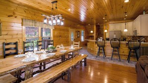 A wooden cabin interior with a dining table set for four, wooden floors, and a kitchen area with bar stools. - Gatlinburg, Hot Tub, Huge Arcade, Dual Racing, Theater, Walk-2-Pool, Free Tix (Gatlinburg)
