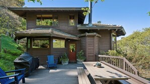 Een houten huis met twee verdiepingen, een terras, buitenzitplaatsen en een overdekte barbecueplek.