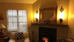 A cozy living room with a fireplace, a sofa, a chair, and a lamp. - Awesome condo, great location, quiet area, completely updated, with wifi.& AC (Ruidoso)