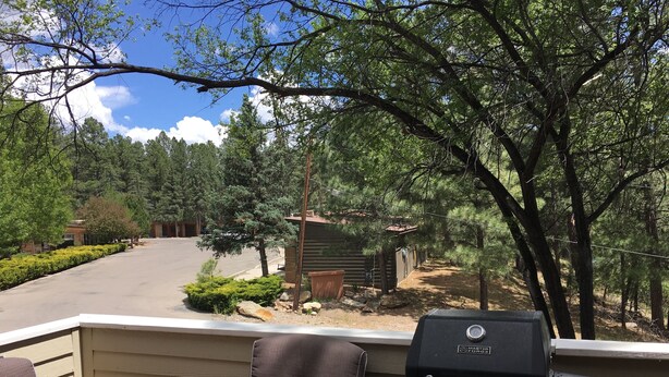 A patio with a grill and two chairs, overlooking a driveway and a wooded area. - Awesome condo, great location, quiet area, completely updated, with wifi.& AC (Ruidoso)